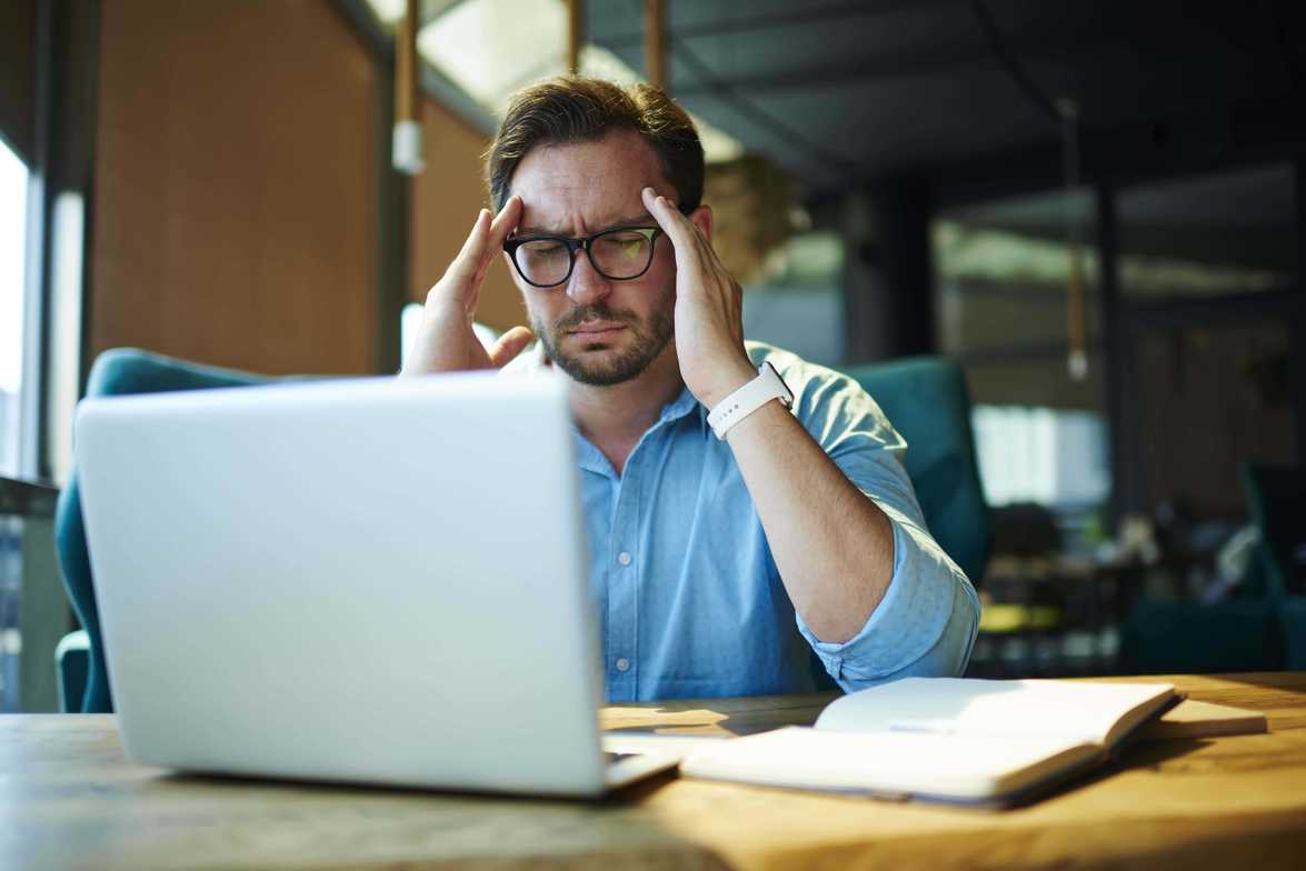 Business owner reviewing financial reports at a desk with laptop and ledger.